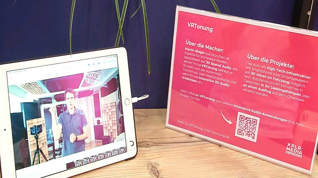 Tablet mit VRTONUNG-Video neben einer Infotafel über 3D Audio im Fahrzeug