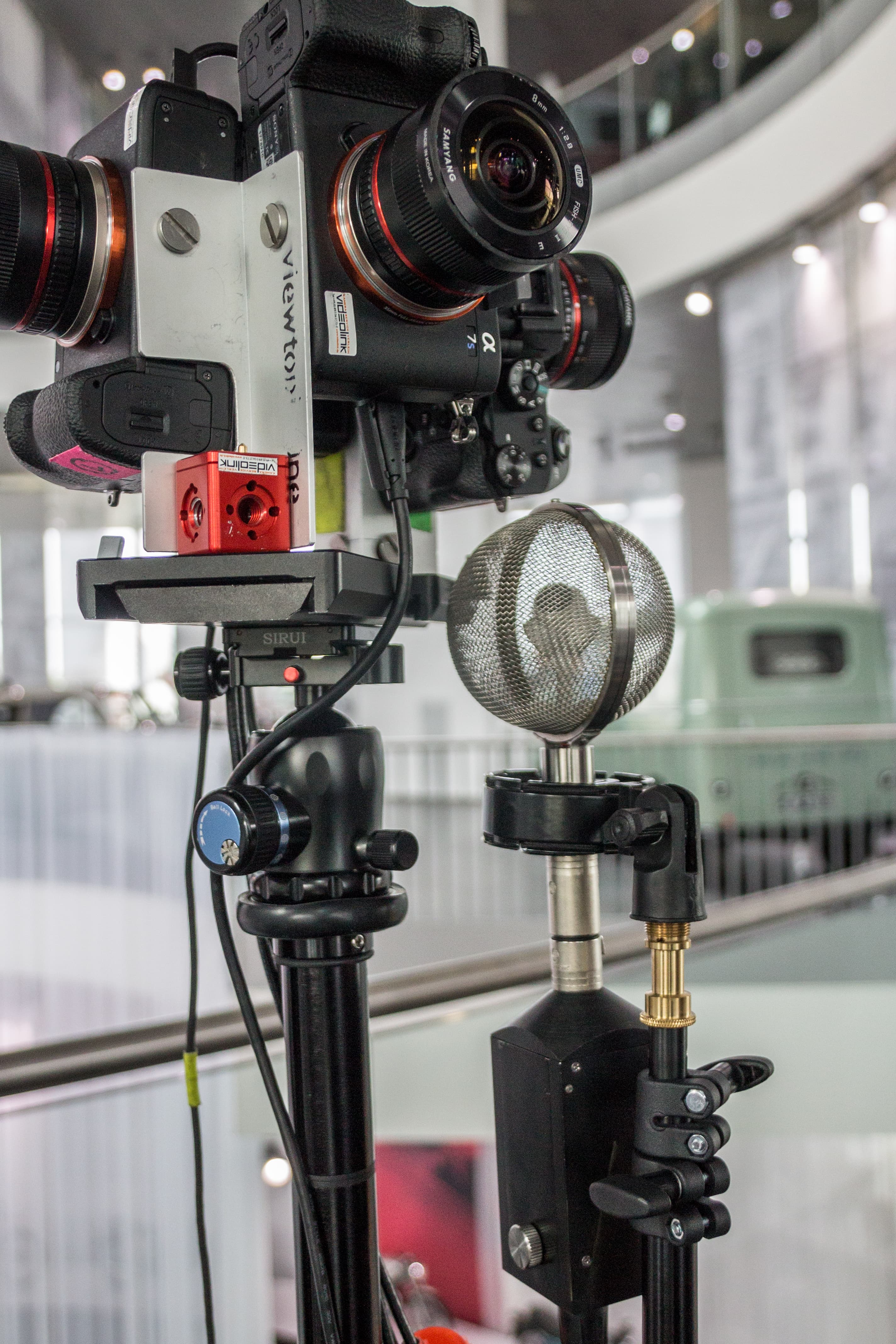 A microphone is placed on a tripod in front of a building for sound engineers utilizing ambisonics.