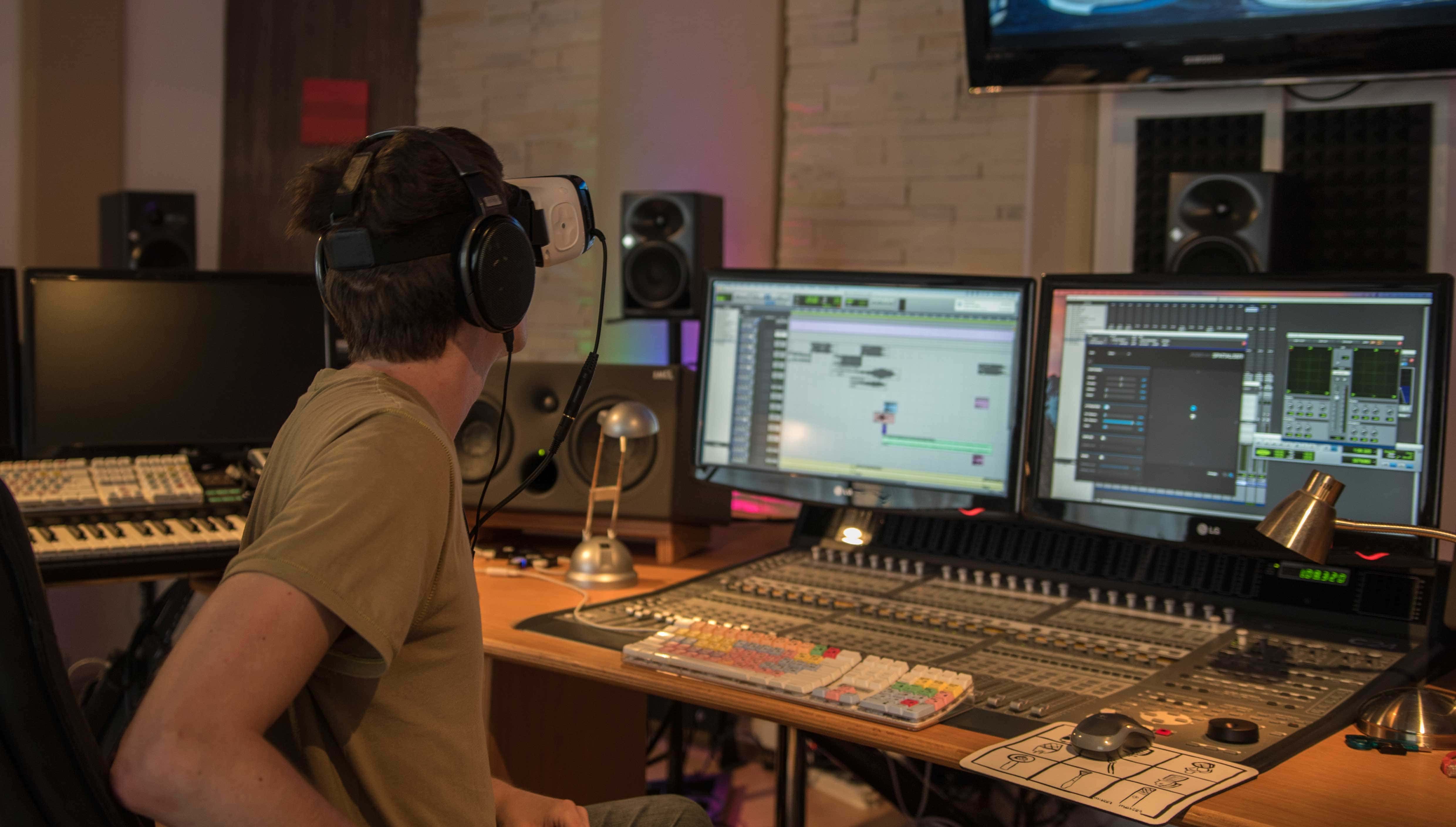 A sound designer sitting behind his monitors doing post production while mixing spatial sound