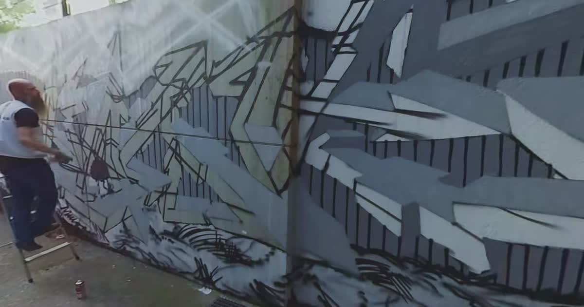 Kuenstler spruehte auf Bodenhoehe ein grossflaechiges graues Graffiti-Piece an eine Wand