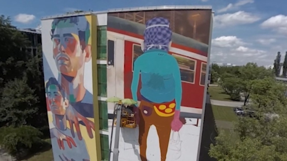 Aerial view of two large murals on a building facade with artists working from a lifting platform