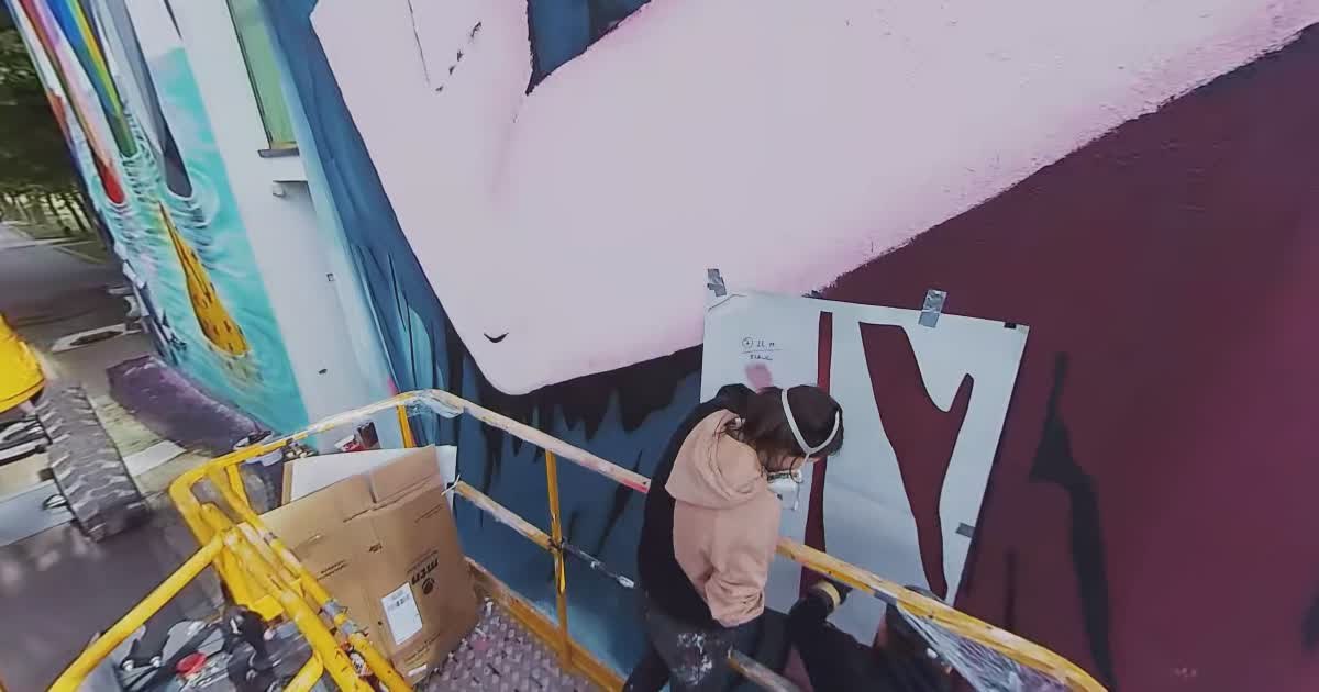 Zwei Kuenstler arbeiten im Arbeitskorb einer Hebebuehne an einem rosa-blauen Wandbild
