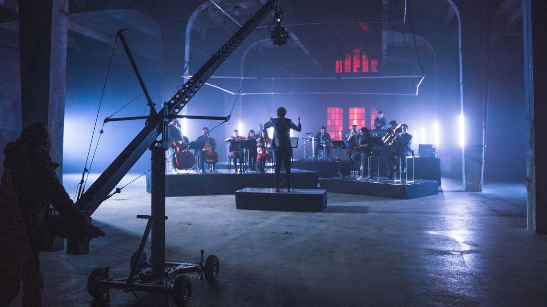 Orchester in einer abgedunkelten Industriehalle, davor ein Kamerakran, rotes Licht im Hintergrund, Dreh zum Markenfilm Audi Symphony