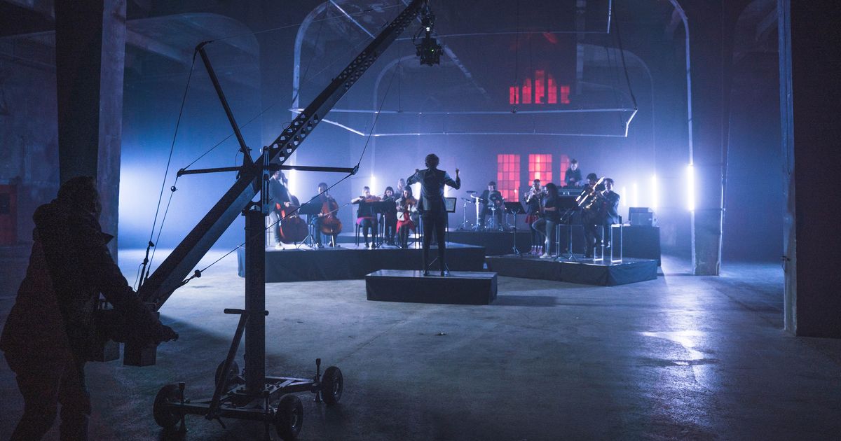 Orchester in einer abgedunkelten Industriehalle, davor ein Kamerakran, rotes Licht im Hintergrund, Dreh zum Markenfilm Audi Symphony