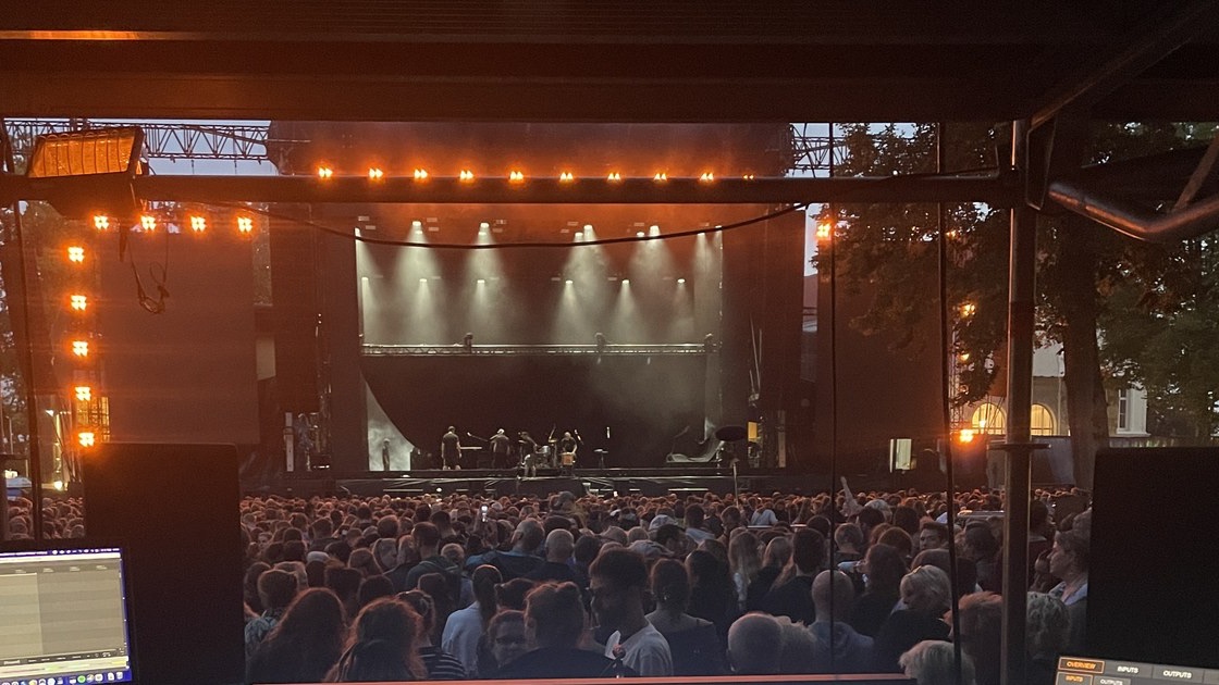 View from the front-of-house desk across the audience onto the lit open-air stage during the concert