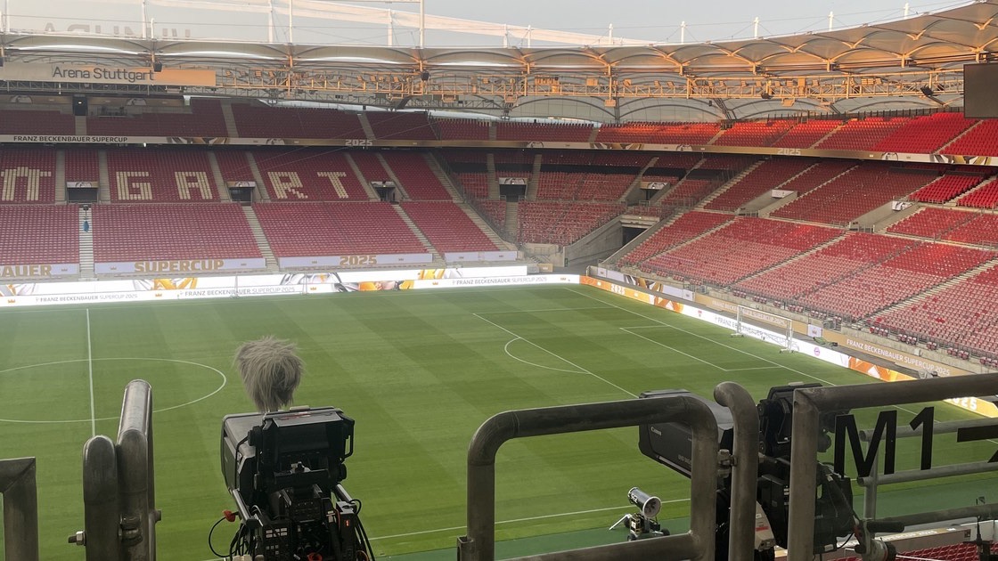 View from the camera position onto the empty pitch of the Arena Stuttgart, with a camera and a microphone in a furry windshield in front