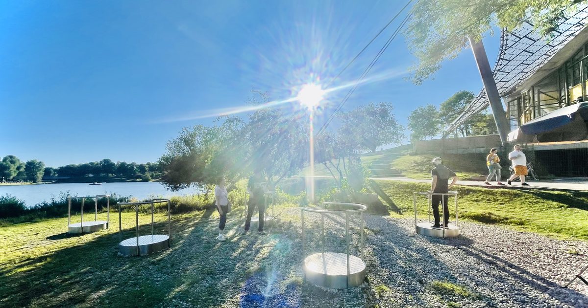 Mehrere Standplattformen auf der Kiesflaeche am Olympiasee, Besucher mit VR-Brillen im Gegenlicht