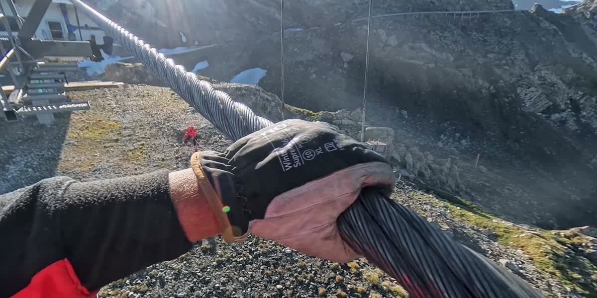 Gloved hand gripping a thick steel rope of a ropeway, POV film still from the 360-degree video
