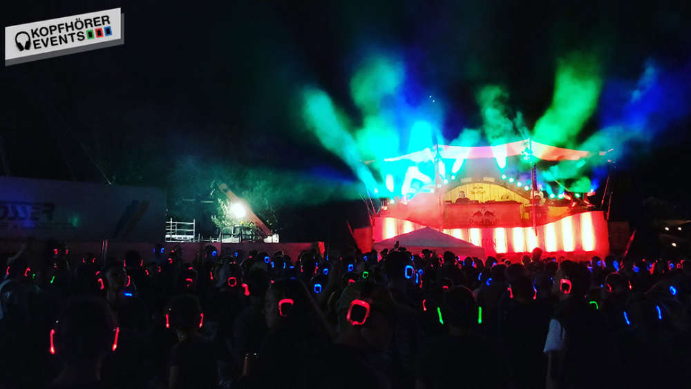 Silent disco crowd with glowing headphones in front of a lit stage