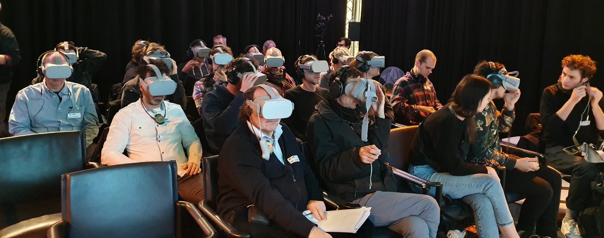 Audience wearing VR headsets and headphones in rows of seats at a VR film screening